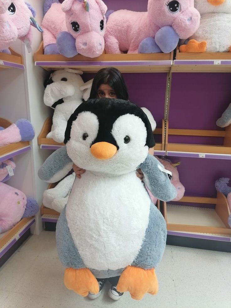 a woman standing in front of shelves with stuffed animals on it's sides and holding onto a penguin