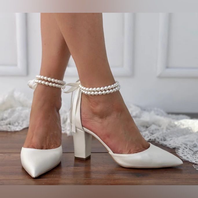 a woman's feet wearing white high heels with pearls on the ankle and heel