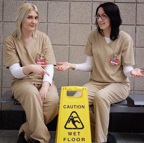 two women in orange prison uniforms sitting next to a caution sign on the ground with their hands out