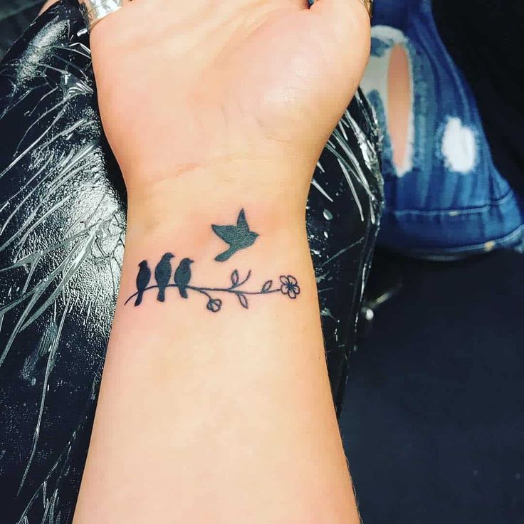 a small tattoo on the wrist of a woman with birds sitting on a tree branch