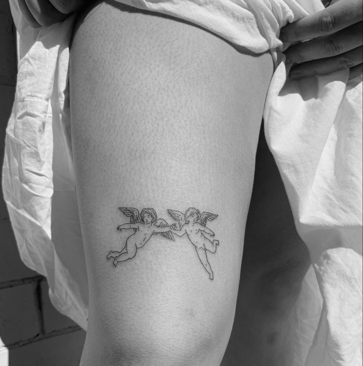 a small tattoo on the leg of a woman with two angels flying over her head