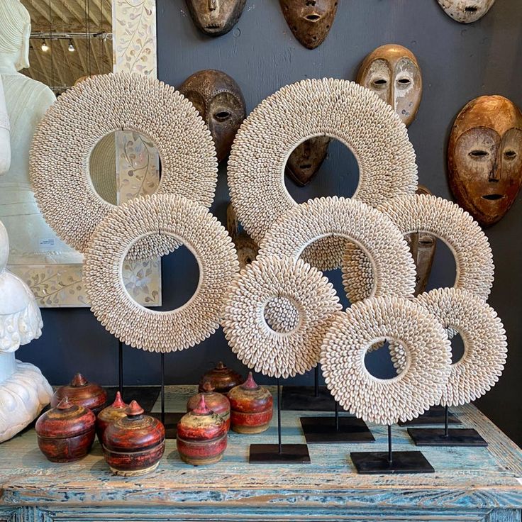 a table topped with lots of different types of vases and masks on the wall