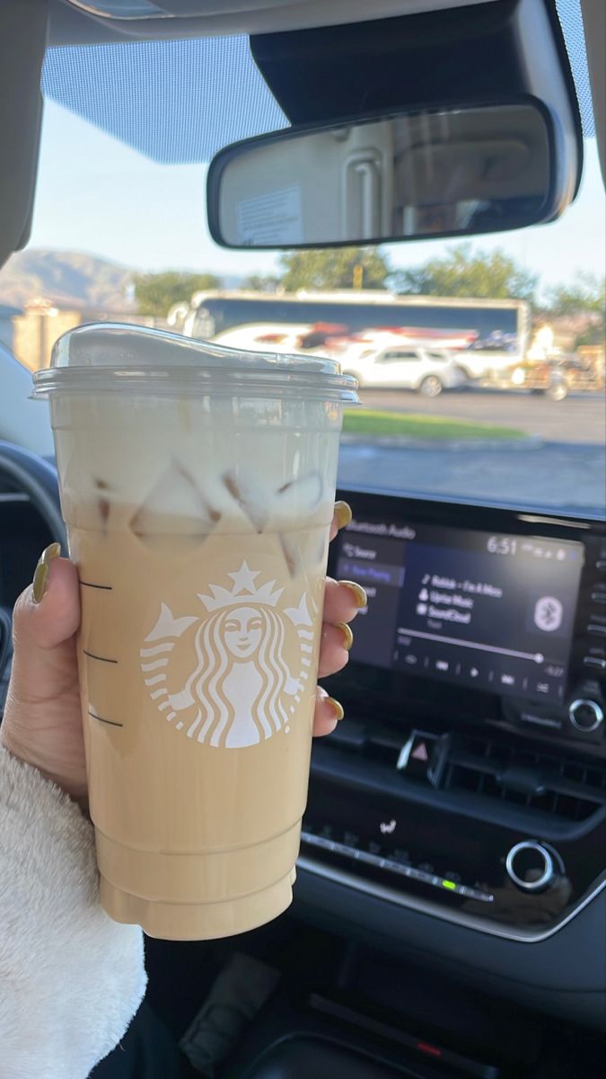 a woman holding up a cup of coffee in her car