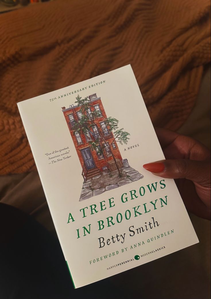 a person holding up a book about a tree grows in brooklyn by betty smith,