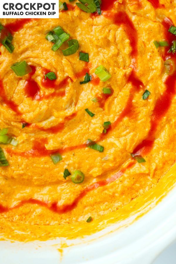 a white bowl filled with carrot hummus and garnished with green onions on top