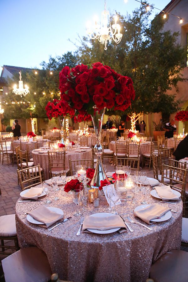 the table is set with white plates and silverware, red roses in vases