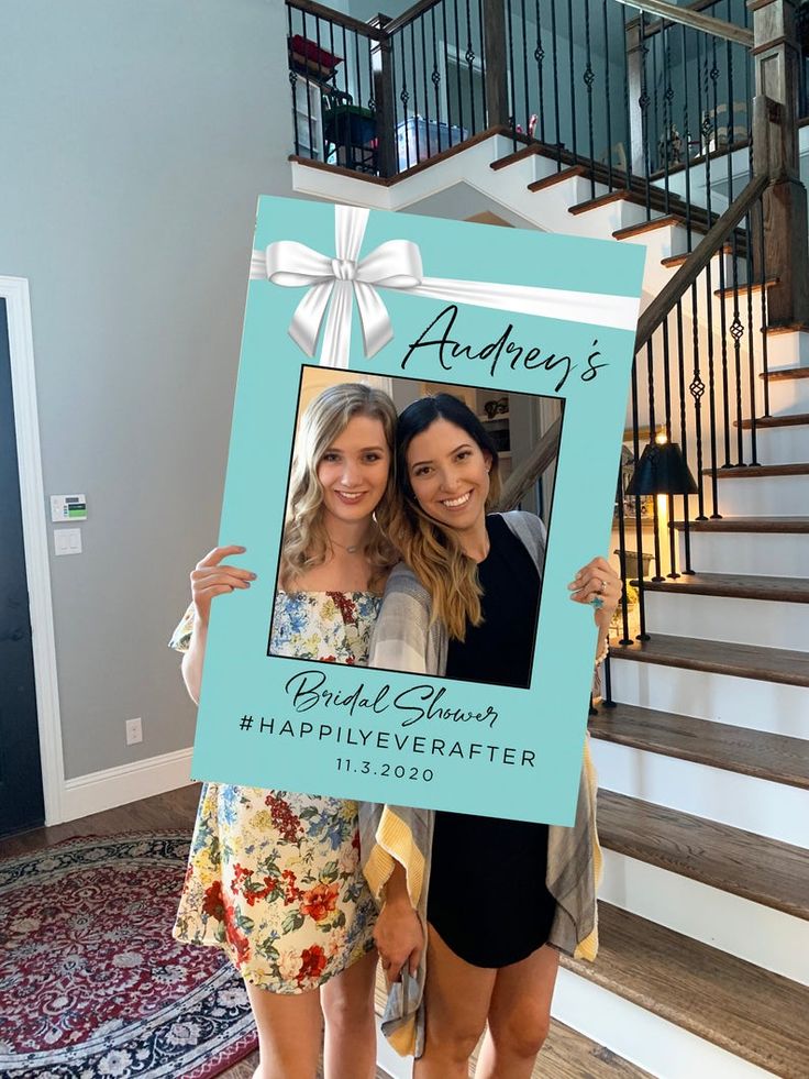 two women standing next to each other in front of stairs holding up a blue frame