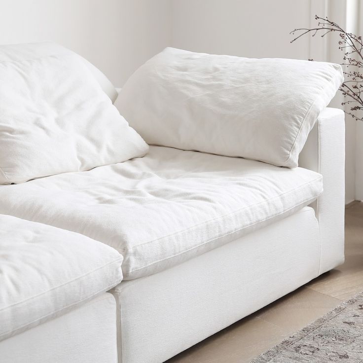 a white couch with pillows on it in front of a rug and window sill