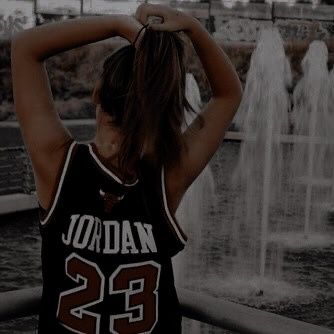 a woman standing in front of a fountain with her hands on her head while wearing a basketball jersey