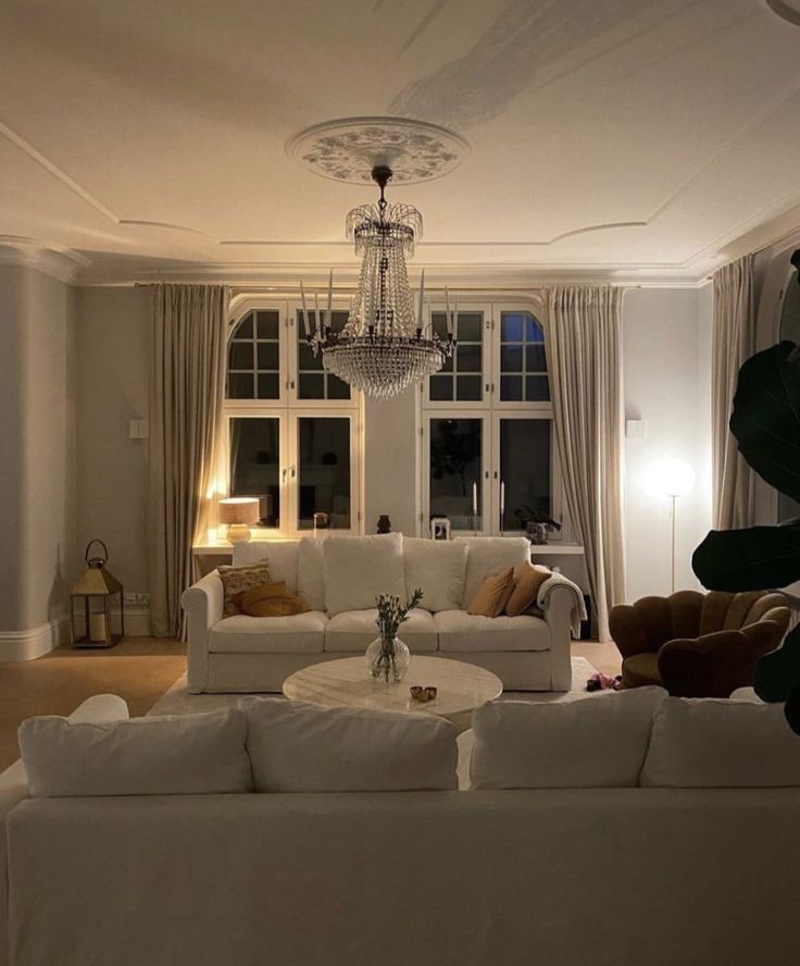 a living room filled with white furniture and a chandelier hanging from the ceiling