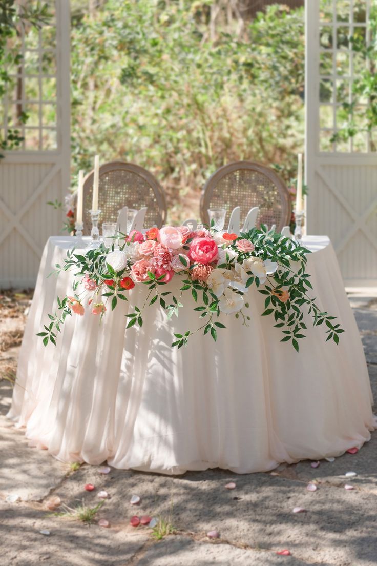 a table with flowers and greenery is set up for an outdoor wedding reception in the shade