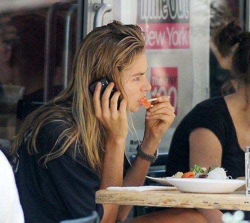 a woman sitting at a table eating food while talking on her cell phone and holding a fork to her mouth