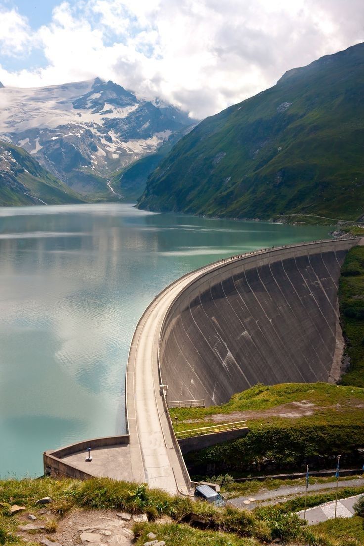 a large body of water with mountains in the background and cars driving along side it