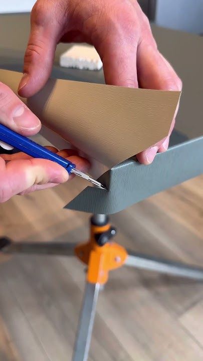 a person cutting paper with scissors on top of a wooden table in front of a camera