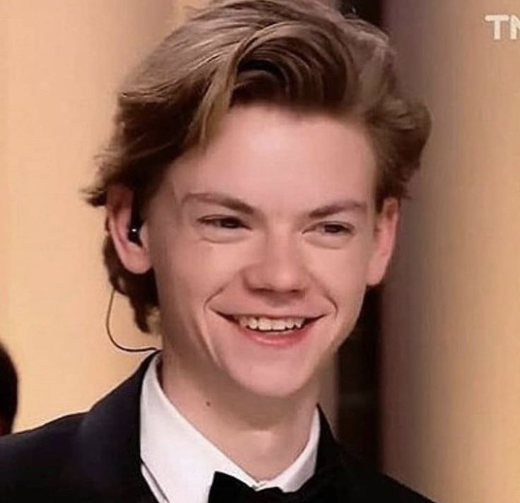 a young man in a tuxedo smiles at the camera while wearing ear buds