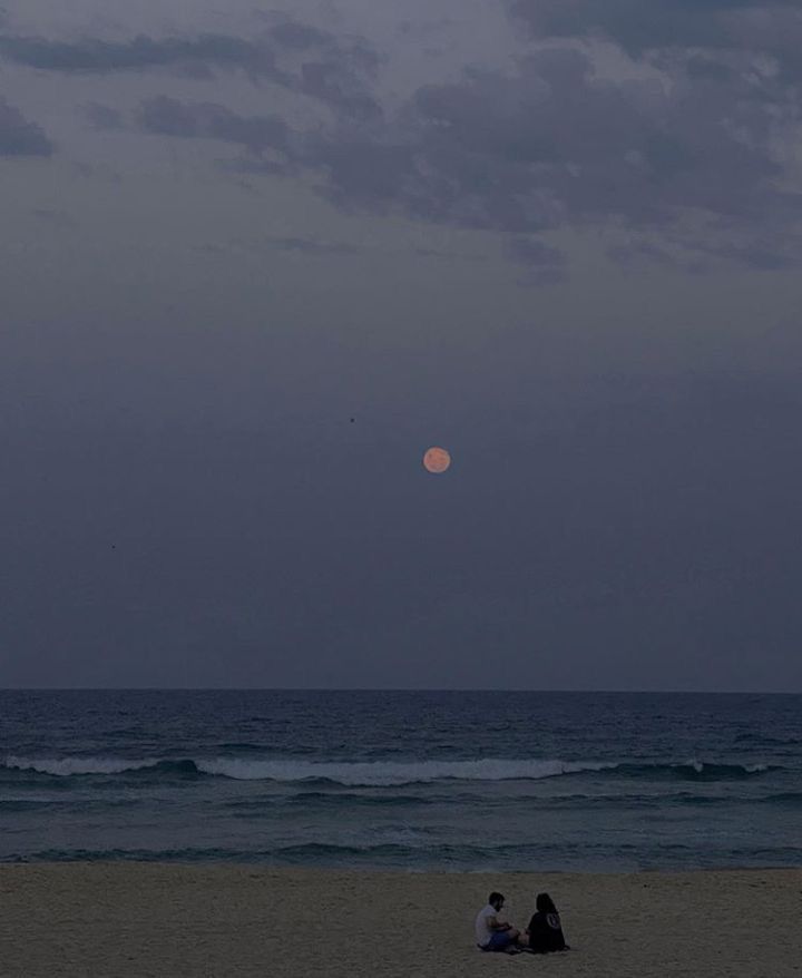 two people sitting on the beach watching the moon