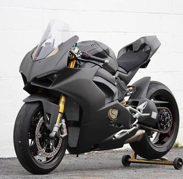 a black motorcycle parked in front of a white brick wall with wheels on each side