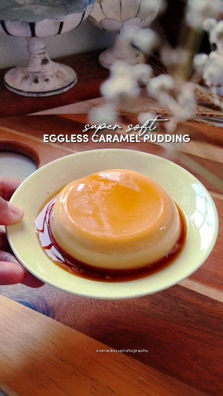 an eggless caramel pudding in a white bowl on a wooden table with flowers