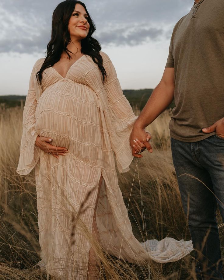 a pregnant woman holding her husband's hand in a field