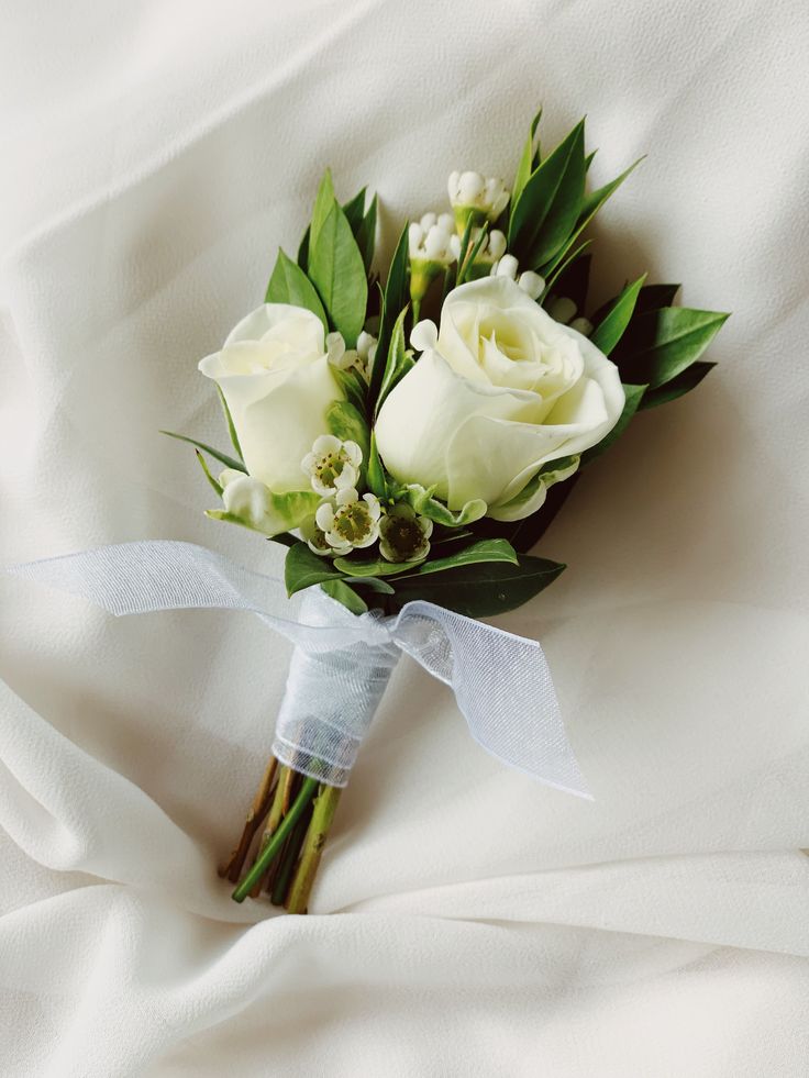 a bridal bouquet with white roses and greenery on a white sheeted bed