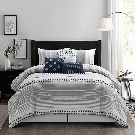 a bed with white and blue comforters in a room next to a lamp on a table