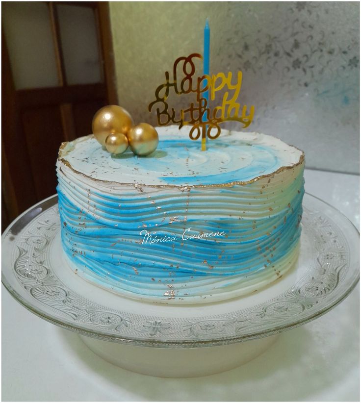 a birthday cake with blue icing and gold decorations on top is sitting on a glass plate