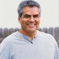 a man with grey hair smiling in front of a wooden fence and white sky background