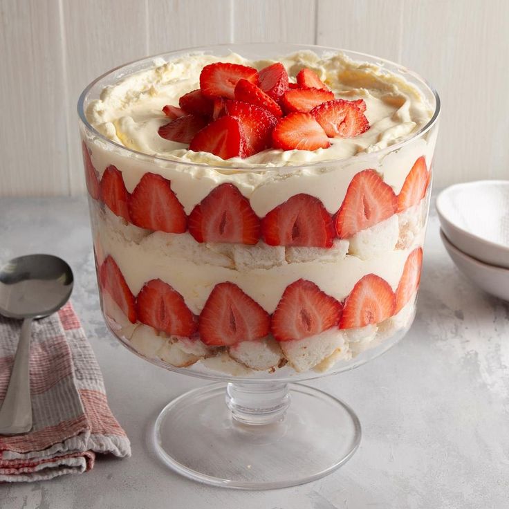 a cake with strawberries on top is in a glass dish next to a spoon