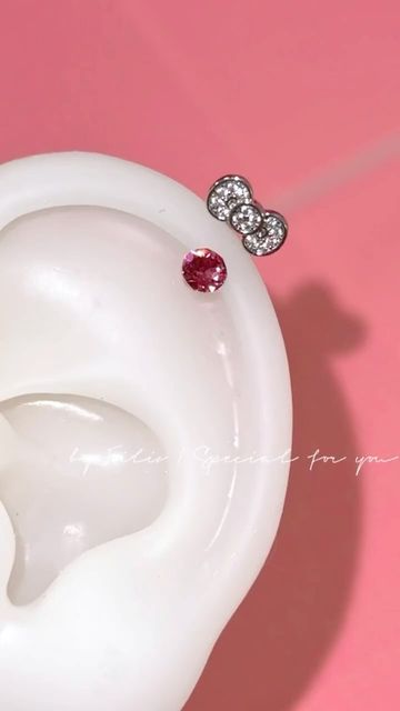 a pair of diamond ear studs sitting on top of a white vase with pink background