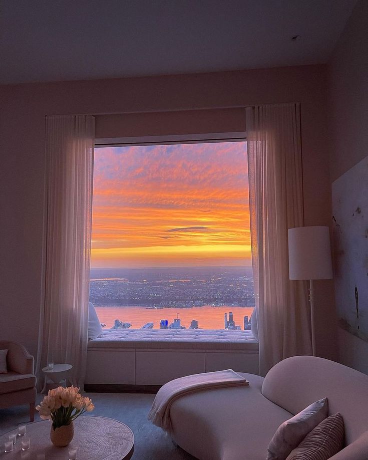 a living room with a large window overlooking the city and water at sunset or sunrise