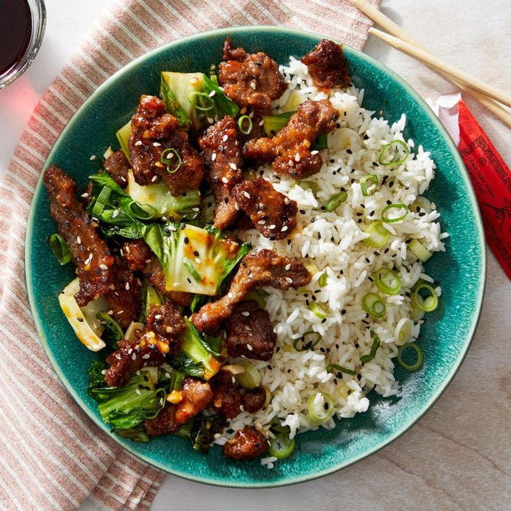 a blue plate topped with meat and rice next to chopsticks on a table