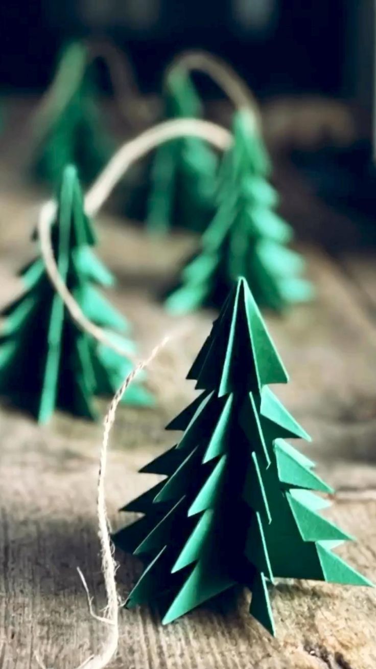 paper christmas trees sitting on top of a wooden table next to twine of twine