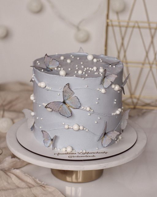 there is a blue cake with white butterflies on the top and pearls on the bottom