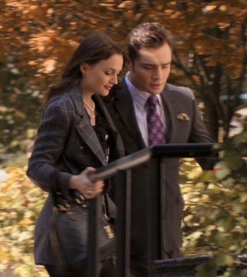 a man and woman standing next to each other in front of trees with leaves on the ground