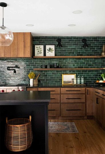 a kitchen with wooden cabinets and green tile backsplash, black countertops, and wood flooring