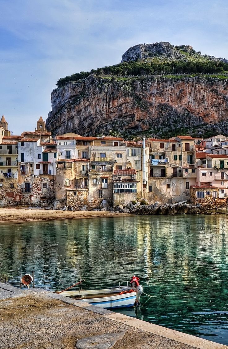 a small boat sits in the water next to an old village on a cliff side