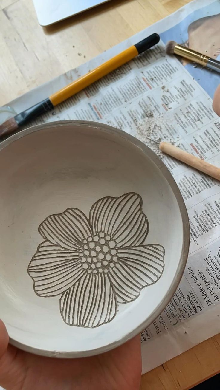 a person is holding a bowl with a flower on it and some crayons