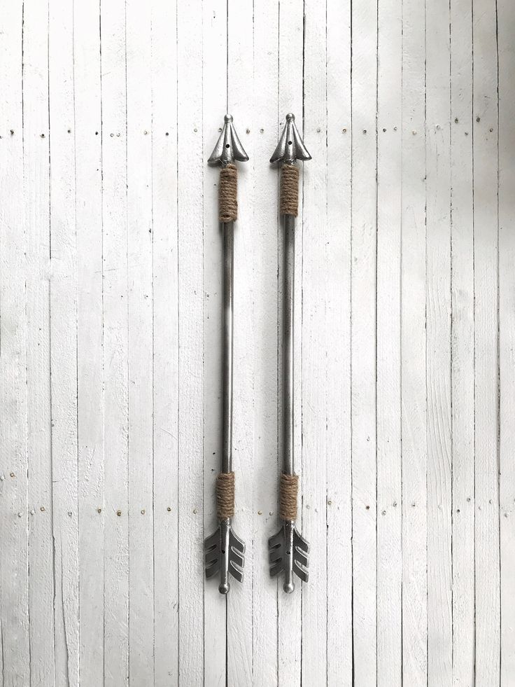 two metal arrows hanging on the side of a white wooden wall next to each other