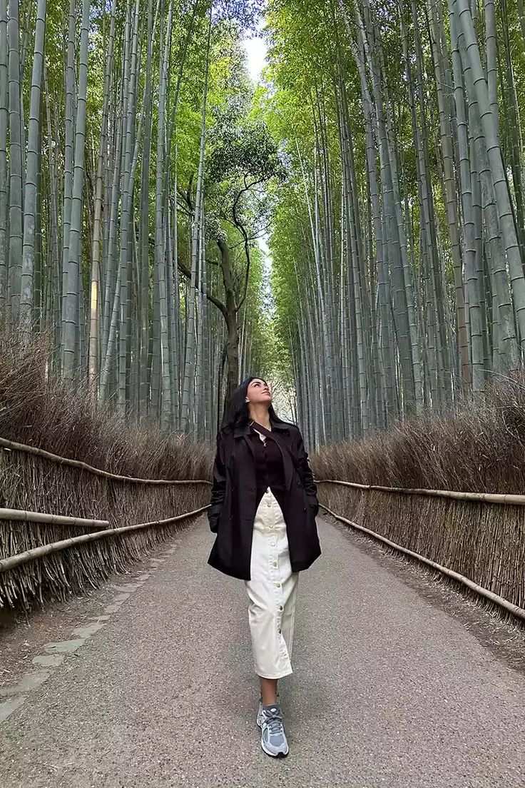 a woman standing in the middle of a road surrounded by tall bamboo trees with her eyes closed