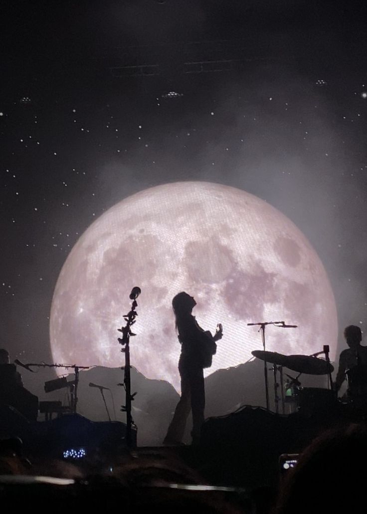 a person standing in front of a full moon with microphones on the side and lights behind them