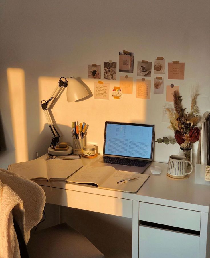 a laptop computer sitting on top of a white desk next to a lamp and chair