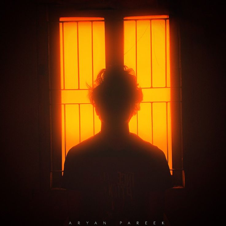 the silhouette of a person standing in front of a window with yellow light coming through it