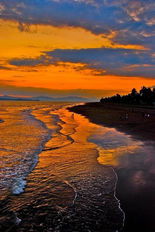 an orange and blue sunset over the ocean with people walking on the beach in the distance