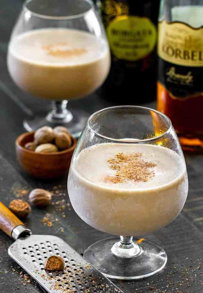 two glasses filled with white wine and nuts on a table next to bottles of alcohol