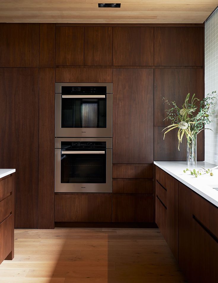 a modern kitchen with wood paneling and stainless steel ovens, counter tops, and sink