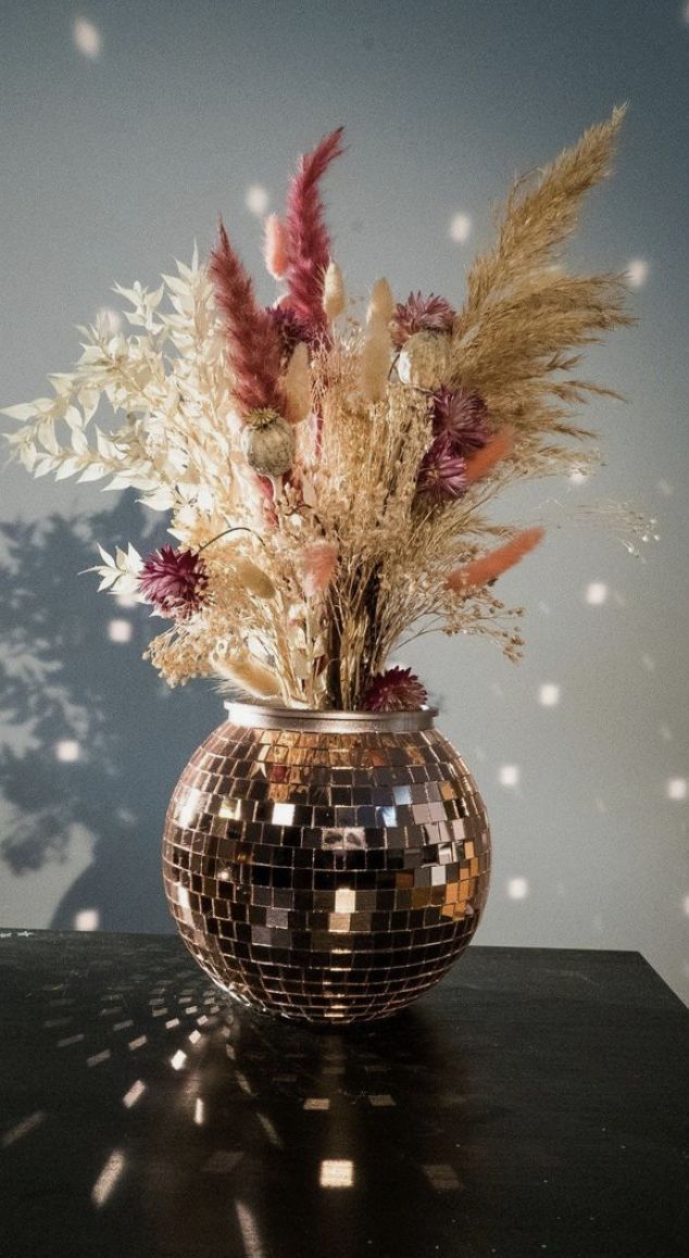 a disco ball vase filled with flowers on top of a black table next to a wall