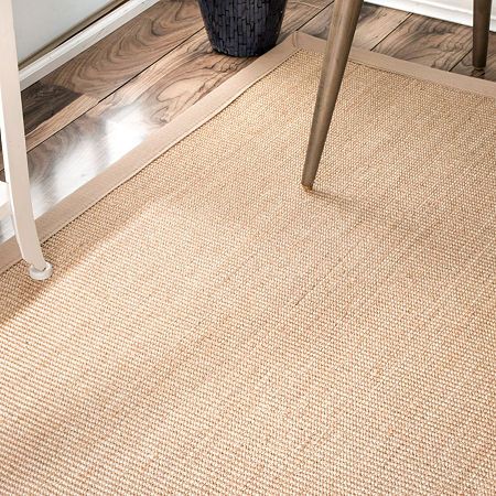 a close up of a rug on the ground near a chair and table with a plant