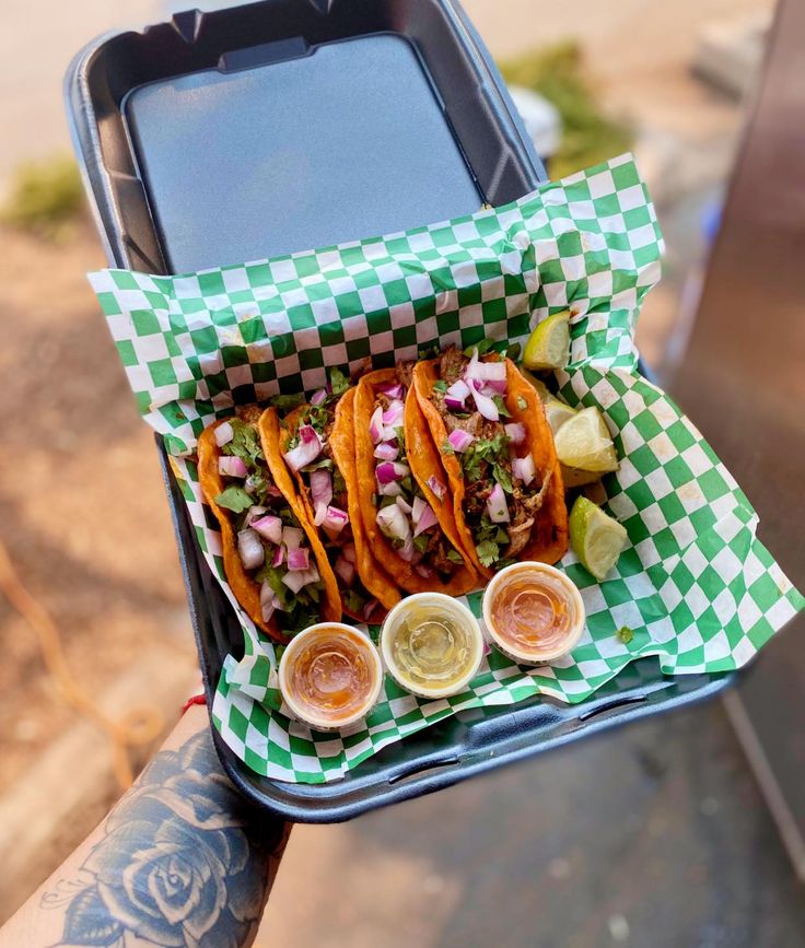 a person holding a tray with three tacos and two dipping sauces on it