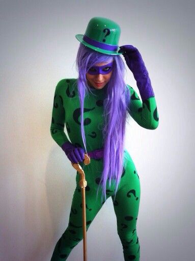 a woman with purple hair wearing a green suit and hat, holding a cane in her hand