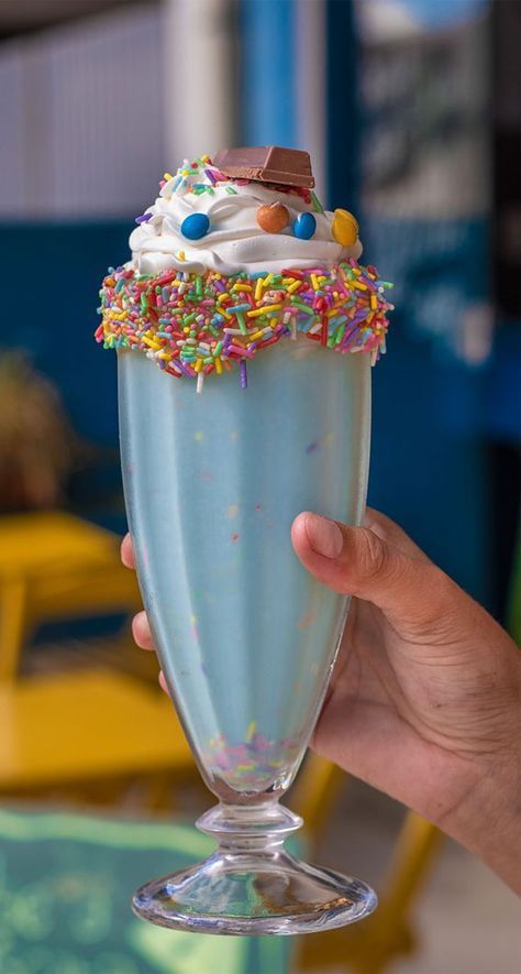 a person holding up a glass with some kind of ice cream and sprinkles on it